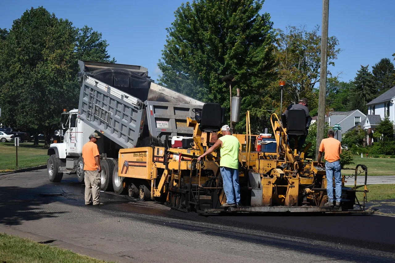 Dump truck delivering hot mix asphalt to a paving machine during a road resurfacing project