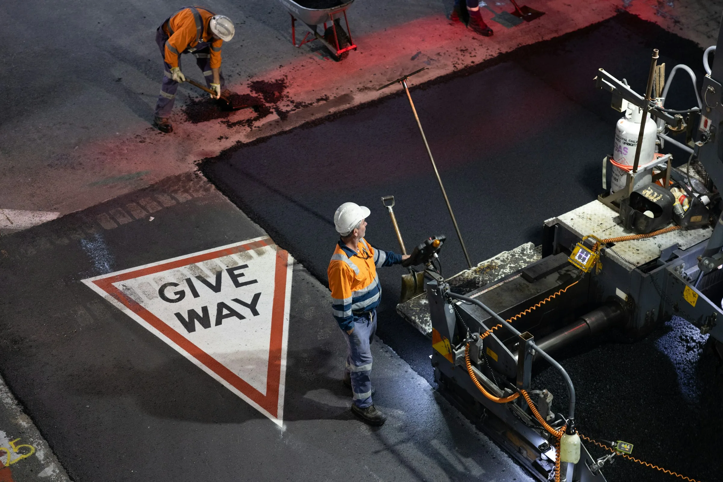 Road crew laying hot mix asphalt at night with a paver machine, illustrating 2026 asphalt price per ton by mix type