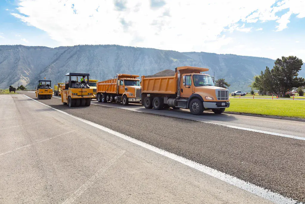 Pneumatic rollers and orange dump trucks laying a chip seal on a road at Mammoth Hot Springs in Yellowstone National Park